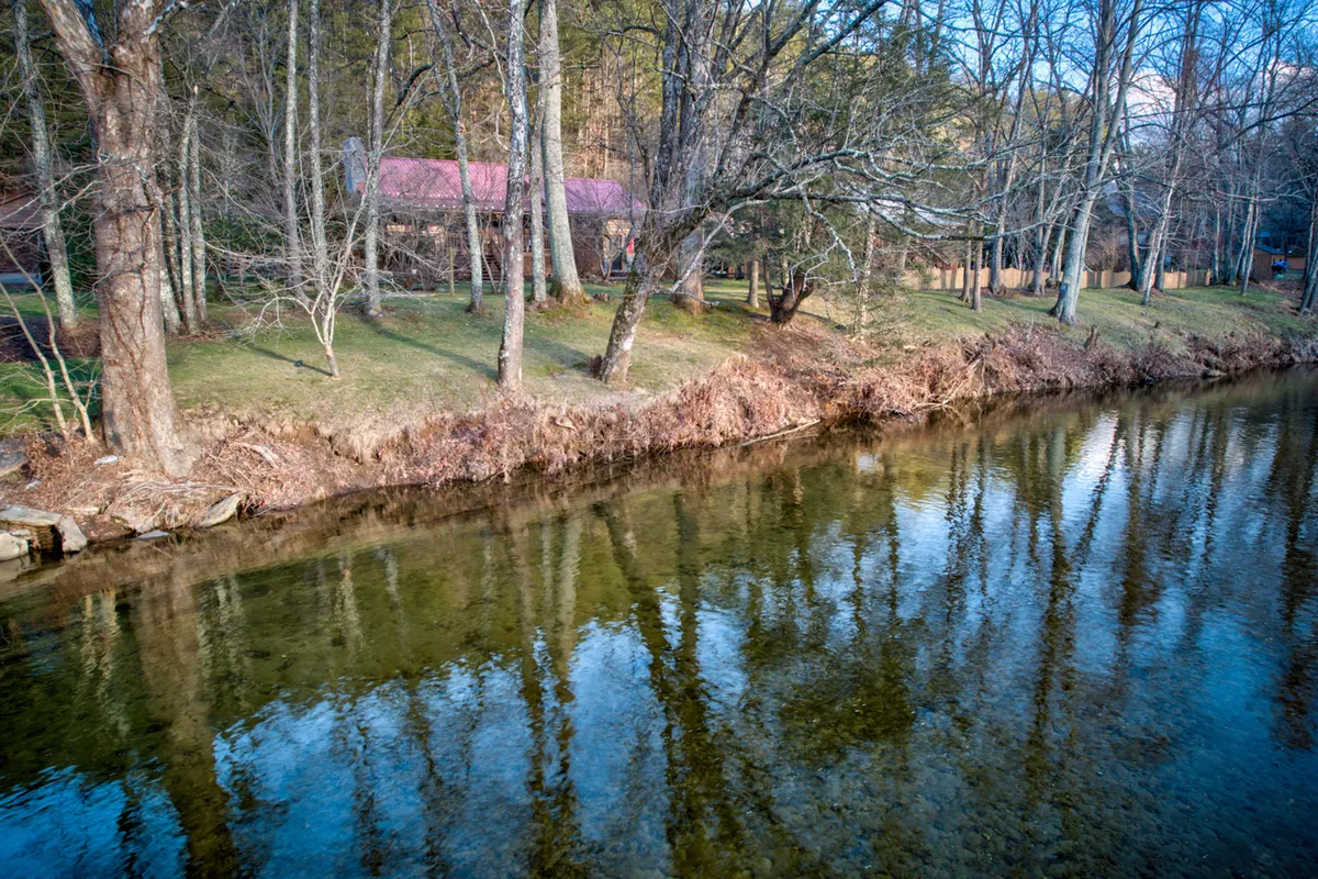 A tranquil riverside scene featuring the house nestled among trees, adjacent to the flowing river. The setting showcases opportunities for fishing, picnicking, and connecting with nature right at the property’s edge.