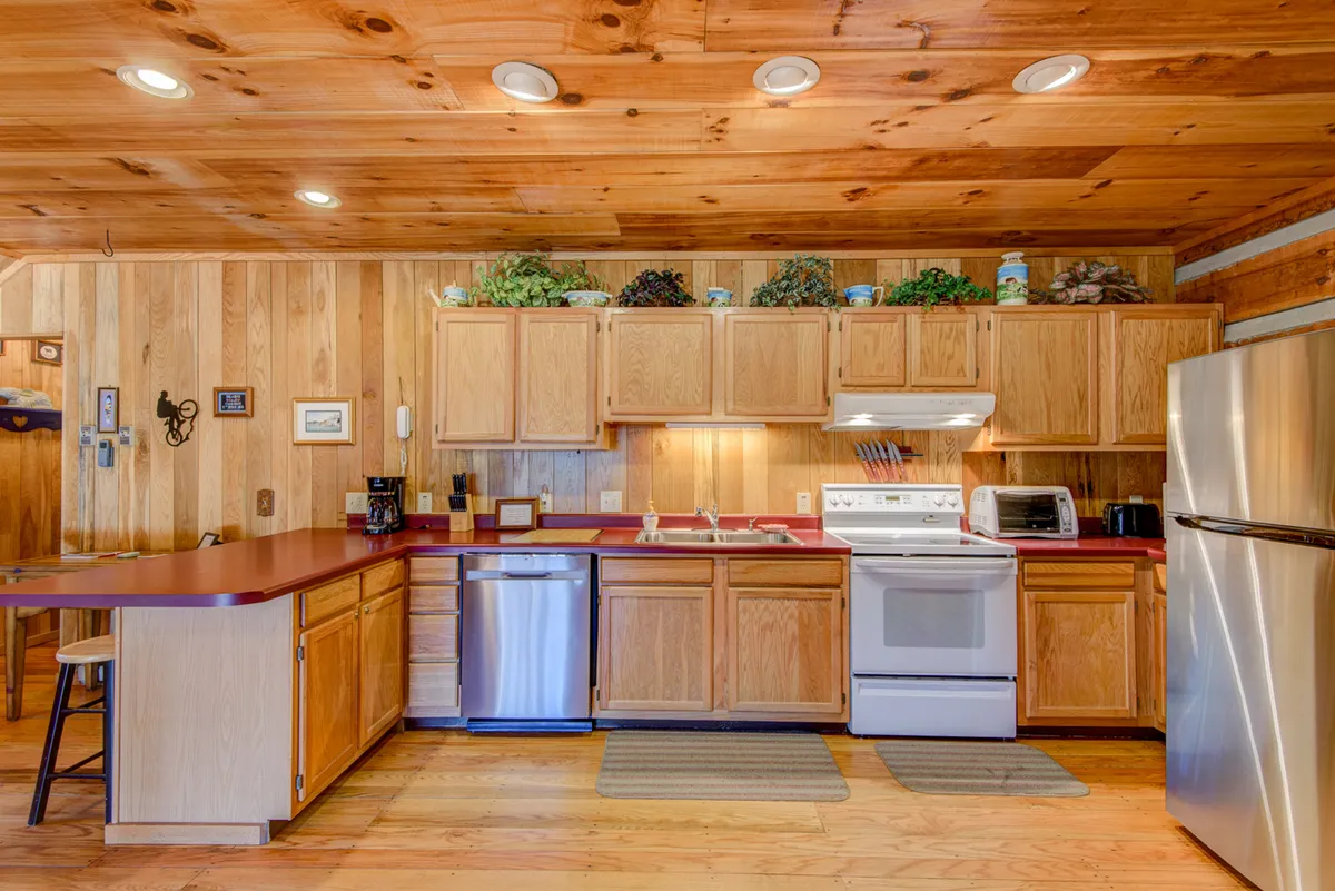 A spacious kitchen with wooden cabinetry, stainless steel appliances, a countertop with bar seating, and decorative plants. The room feels open and ready for meal preparation or social gatherings, with plenty of space for family activities.