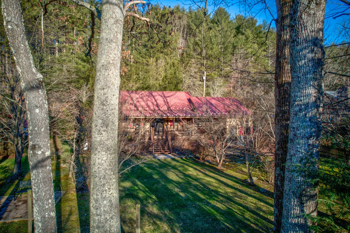 An inviting exterior view of a home with a red metal roof, wooden porch, and surrounding trees. The porch looks like a perfect spot for stargazing, morning coffee, or gathering with friends and family after outdoor adventures.