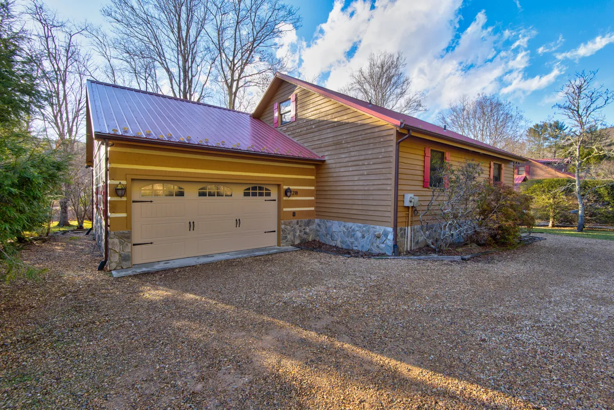 An exterior view showing a garage with double doors, wooden siding, a red roof, and a landscaped garden. This image hints at parking arrangements and access to the home in all seasons, with space for vehicles and a clear, accessible entrance.