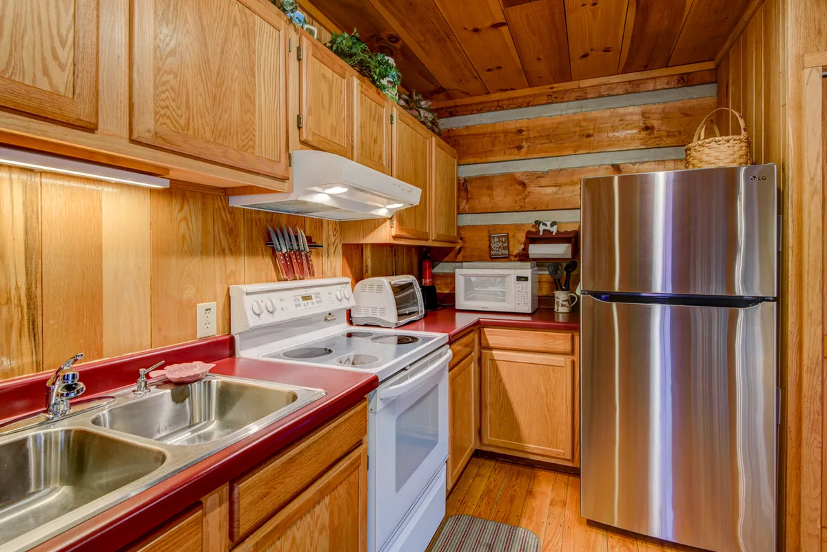 A functional kitchen with stainless steel refrigerator, white stove and oven, wooden cabinetry, and a red countertop. Kitchen utensils are neatly arranged, suggesting the space is well-equipped for meal preparation and daily routines.