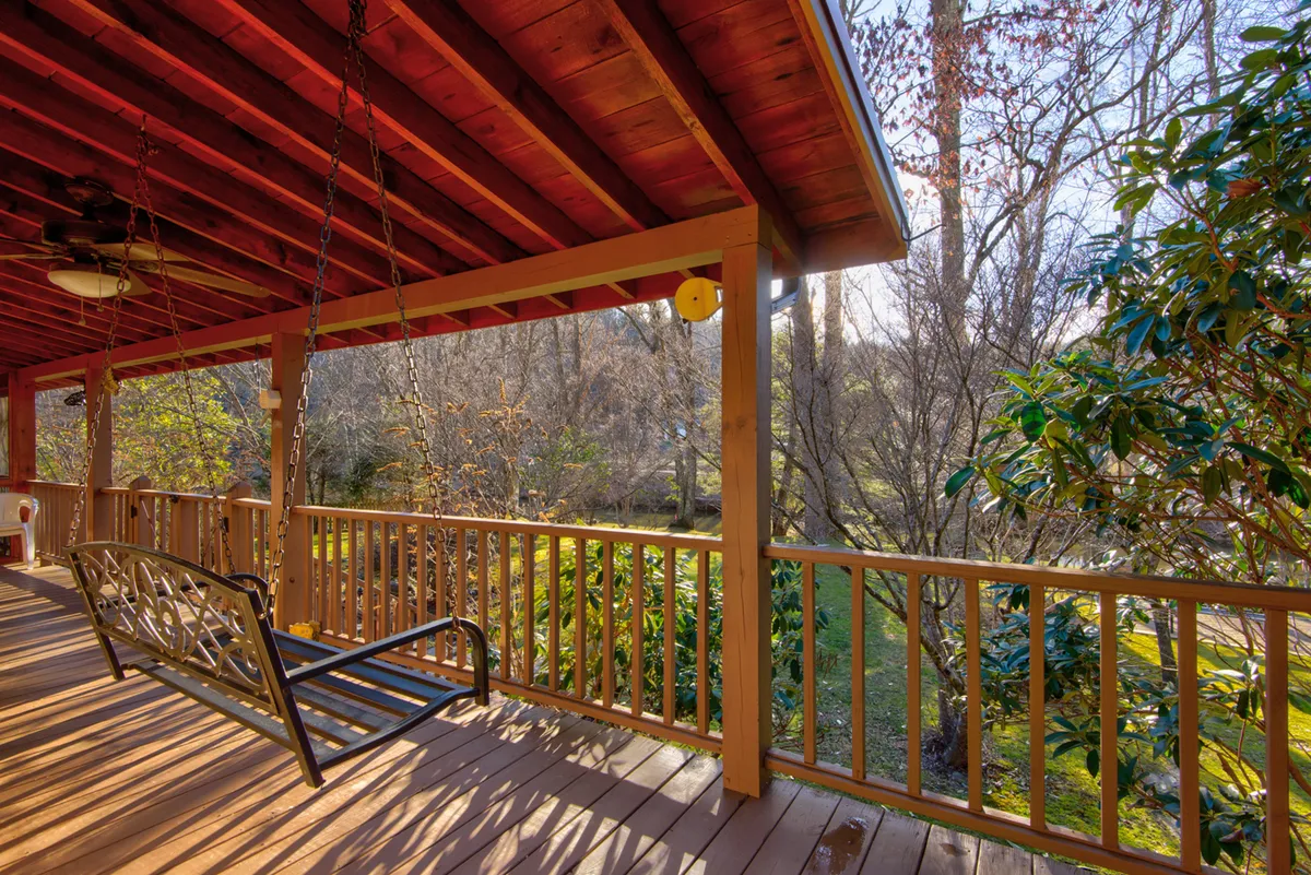 A wooden porch with a swinging bench surrounded by lush greenery, offering a view of the serene outdoors. The porch provides a cozy spot to relax with pets while enjoying the sounds and sights of nature.