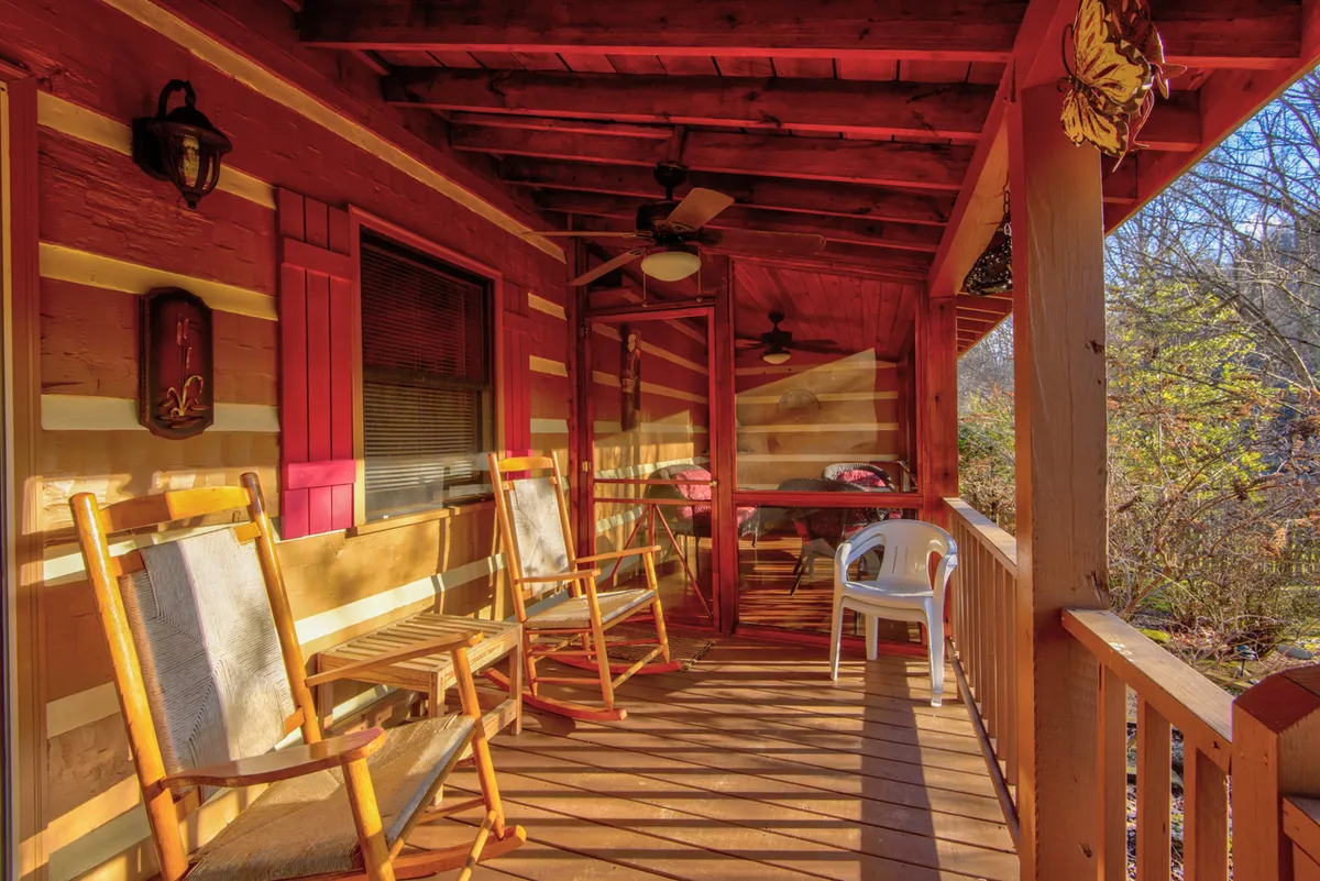 A cozy exterior porch with rocking chairs, wooden railings, colorful shutters, and a ceiling fan. The porch overlooks natural surroundings, embodying a welcoming spot for morning coffee, wildlife watching, or unwinding after a day outdoors.